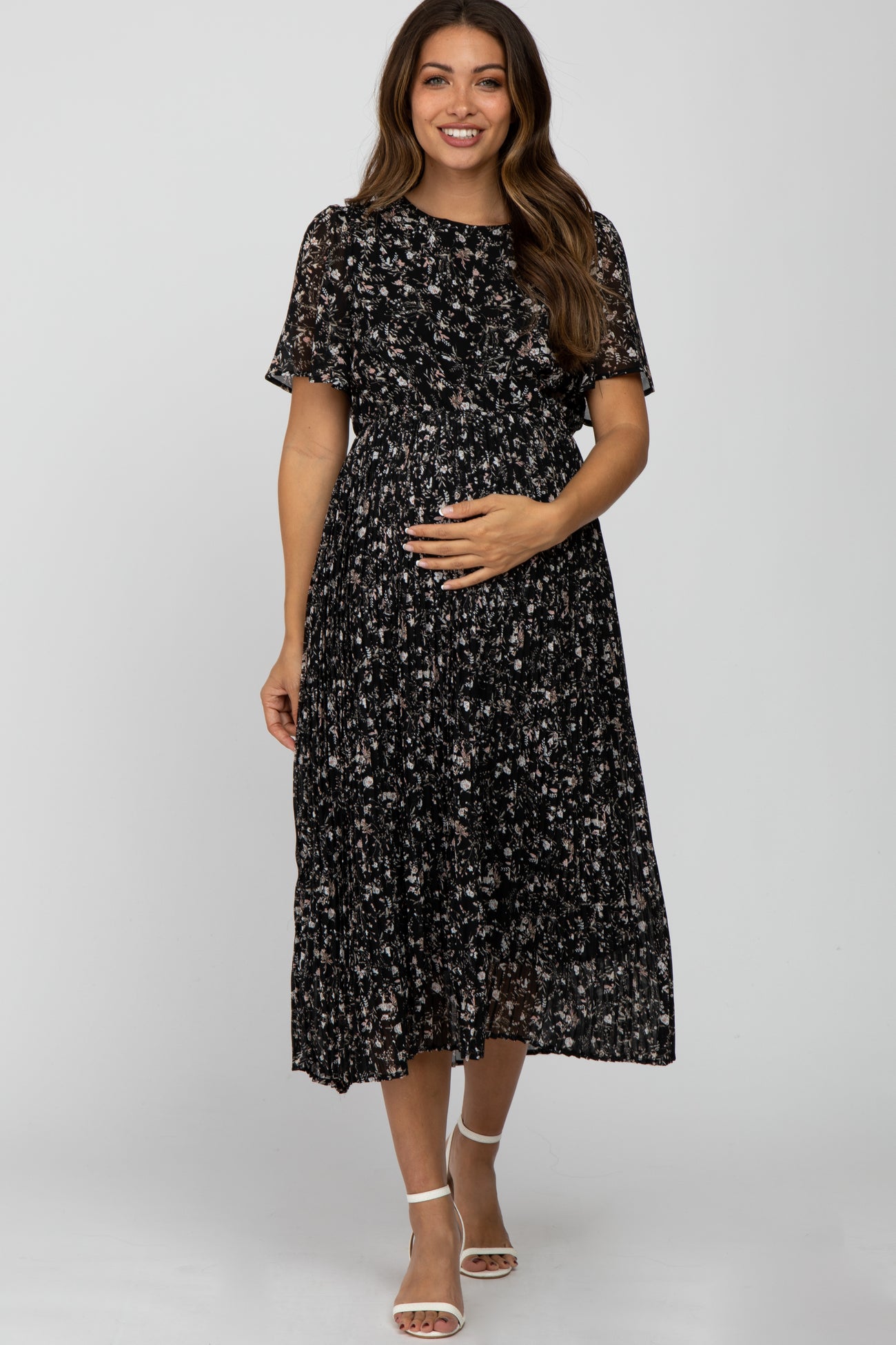 woman wearing a black floral print maternity dress with short sleeves and a flowing skirt, holding her baby bump
