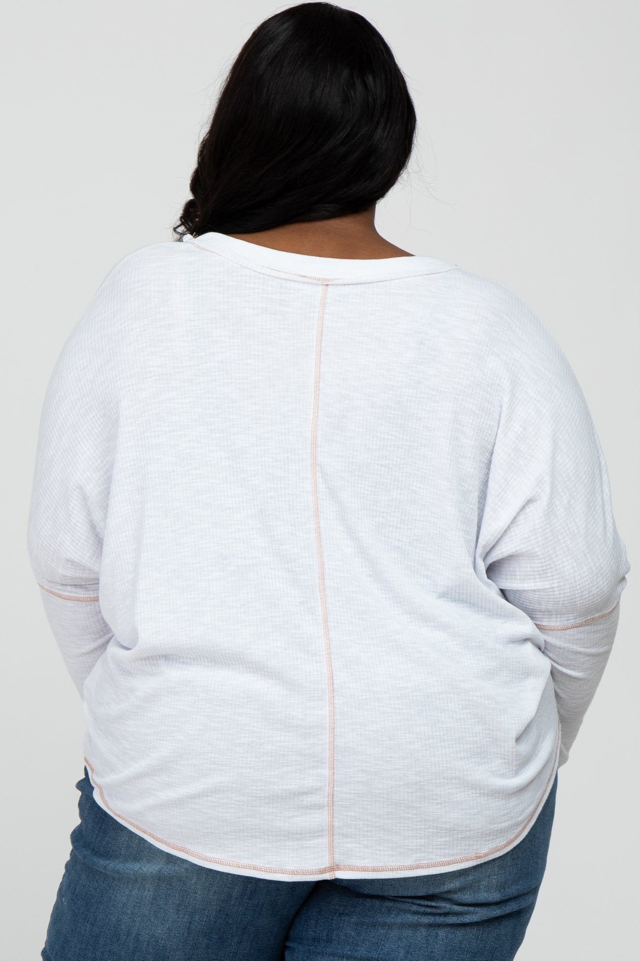Back view of a person wearing a white long-sleeve waffle knit top with exposed seam detailing and blue jeans