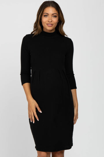Pregnant woman wearing a black long-sleeve turtleneck maternity dress against a white background