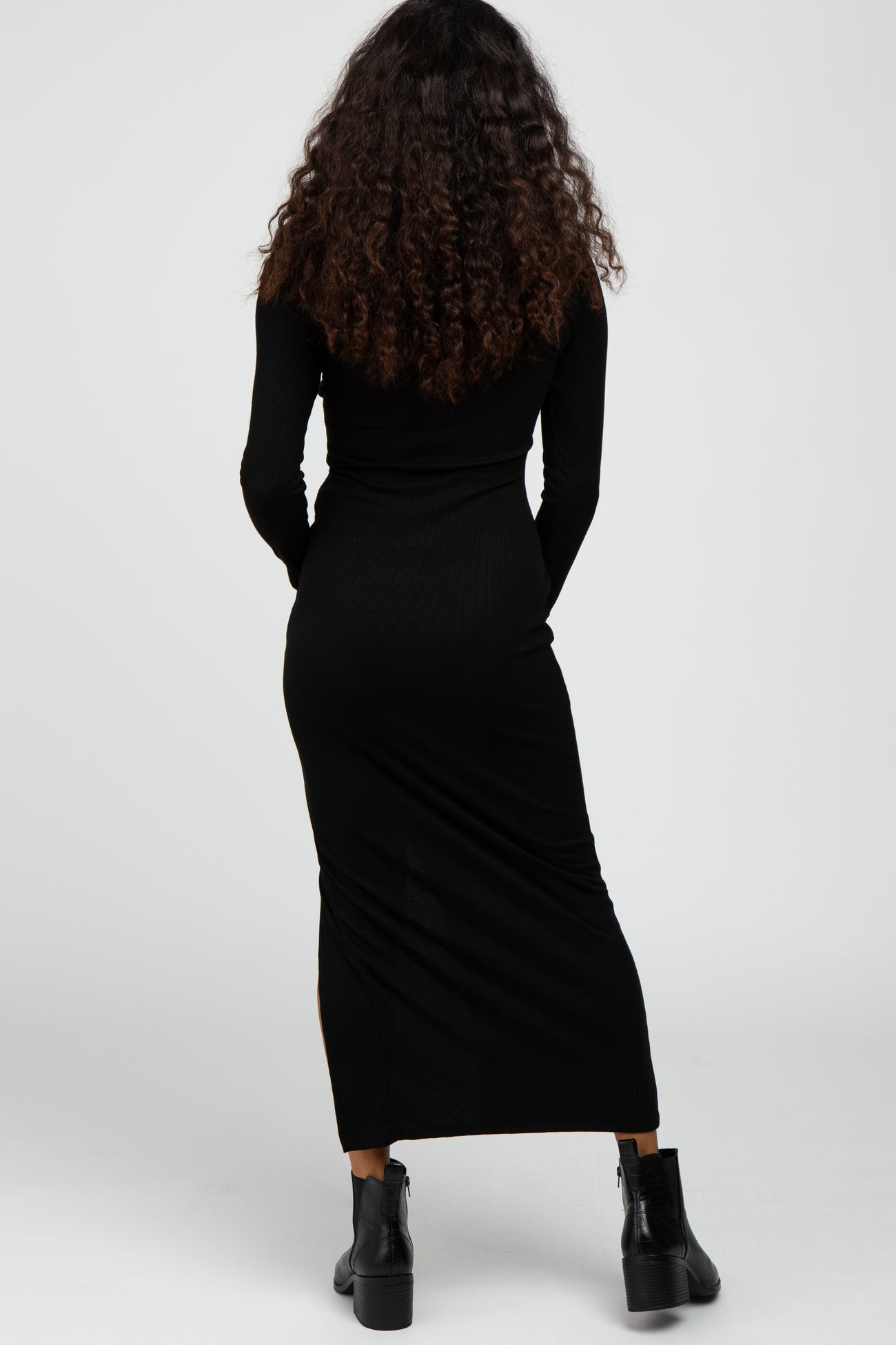 woman wearing a fitted black long sleeve maxi dress, showing the back view, styled with black ankle boots