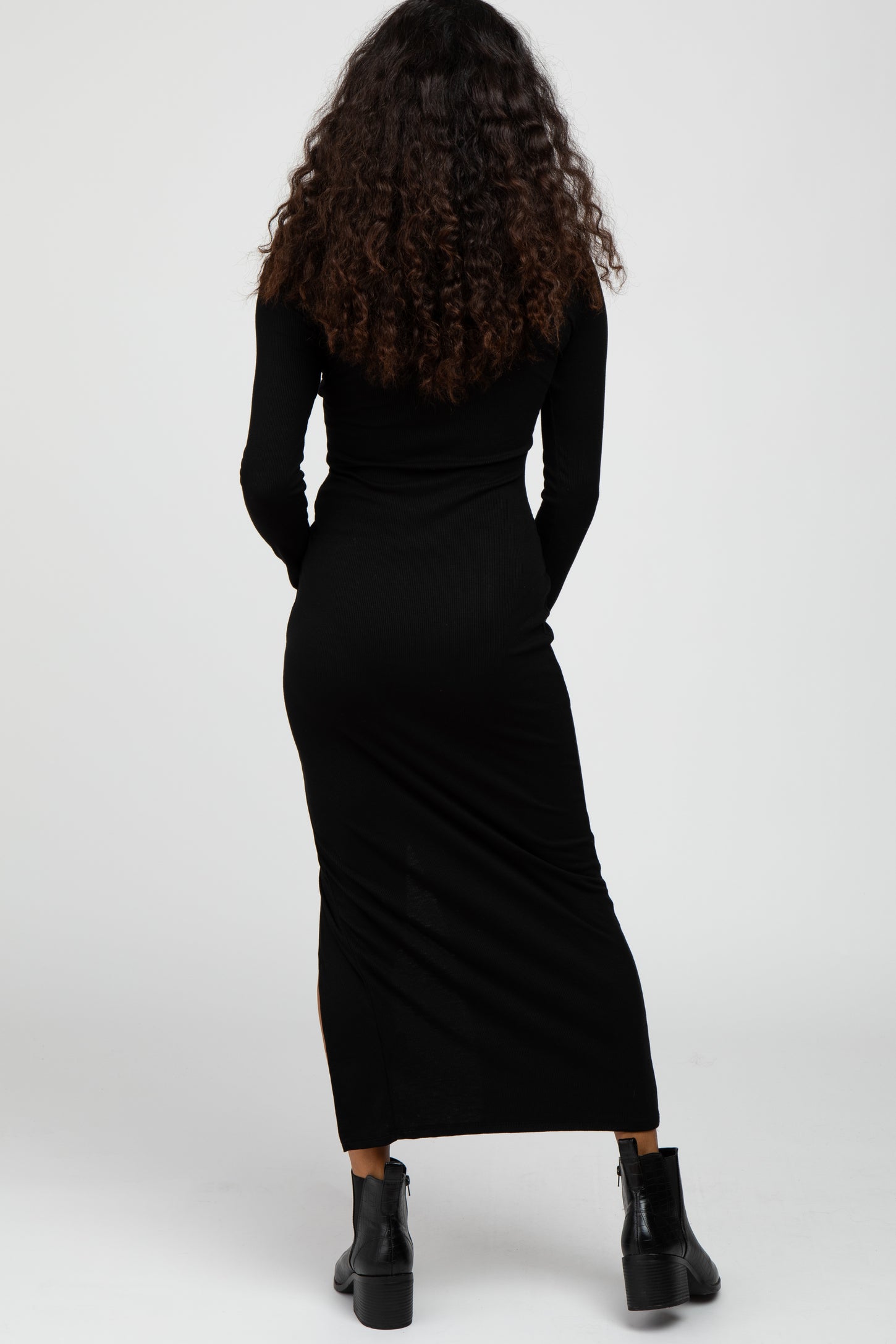 woman wearing a fitted black long sleeve maxi dress, showing the back view, styled with black ankle boots