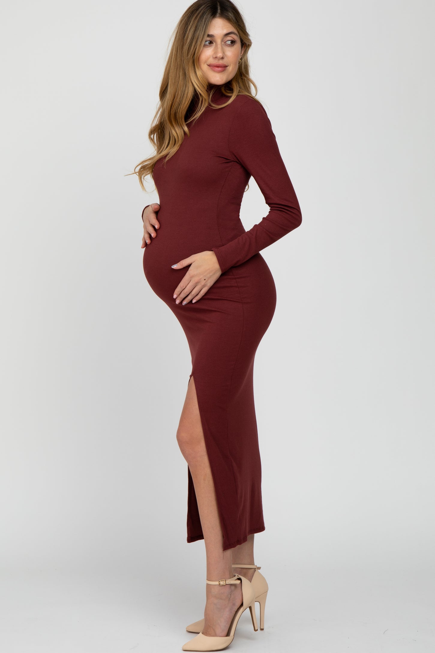 woman wearing a burgundy long sleeve maternity dress with a side slit and holding her baby bump