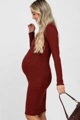 woman wearing a burgundy ribbed long sleeve maternity dress showcasing her baby bump and holding a handbag