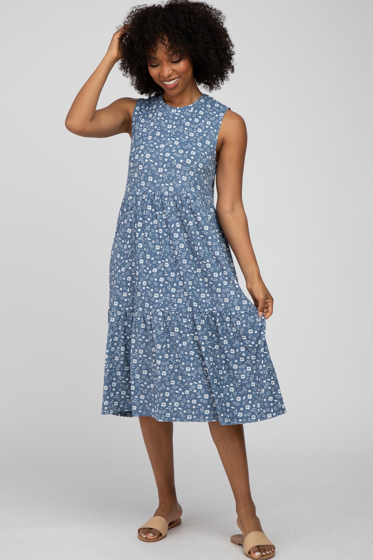 woman wearing a blue sleeveless tiered midi dress with white floral print and tan slide sandals