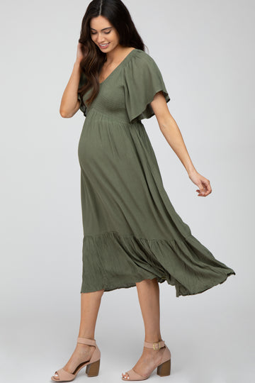woman wearing a green maternity dress with flutter sleeves and a flowing skirt, showcasing her baby bump