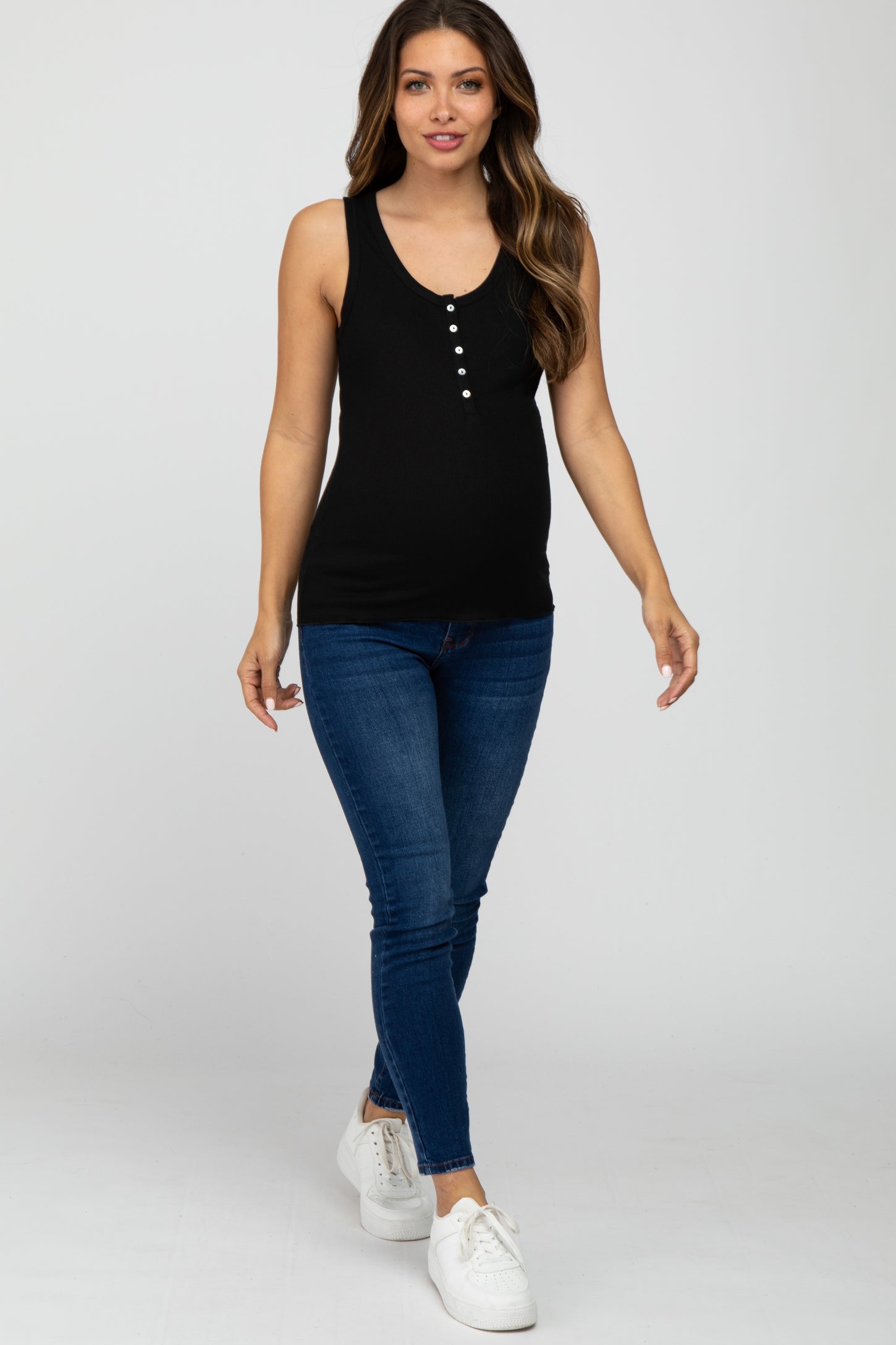 woman wearing a black maternity tank top with buttons and blue skinny jeans, showcasing her baby bump
