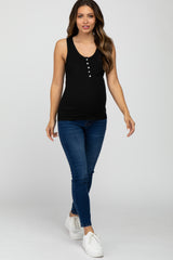 woman wearing a black maternity tank top with buttons and blue skinny jeans, showcasing her baby bump