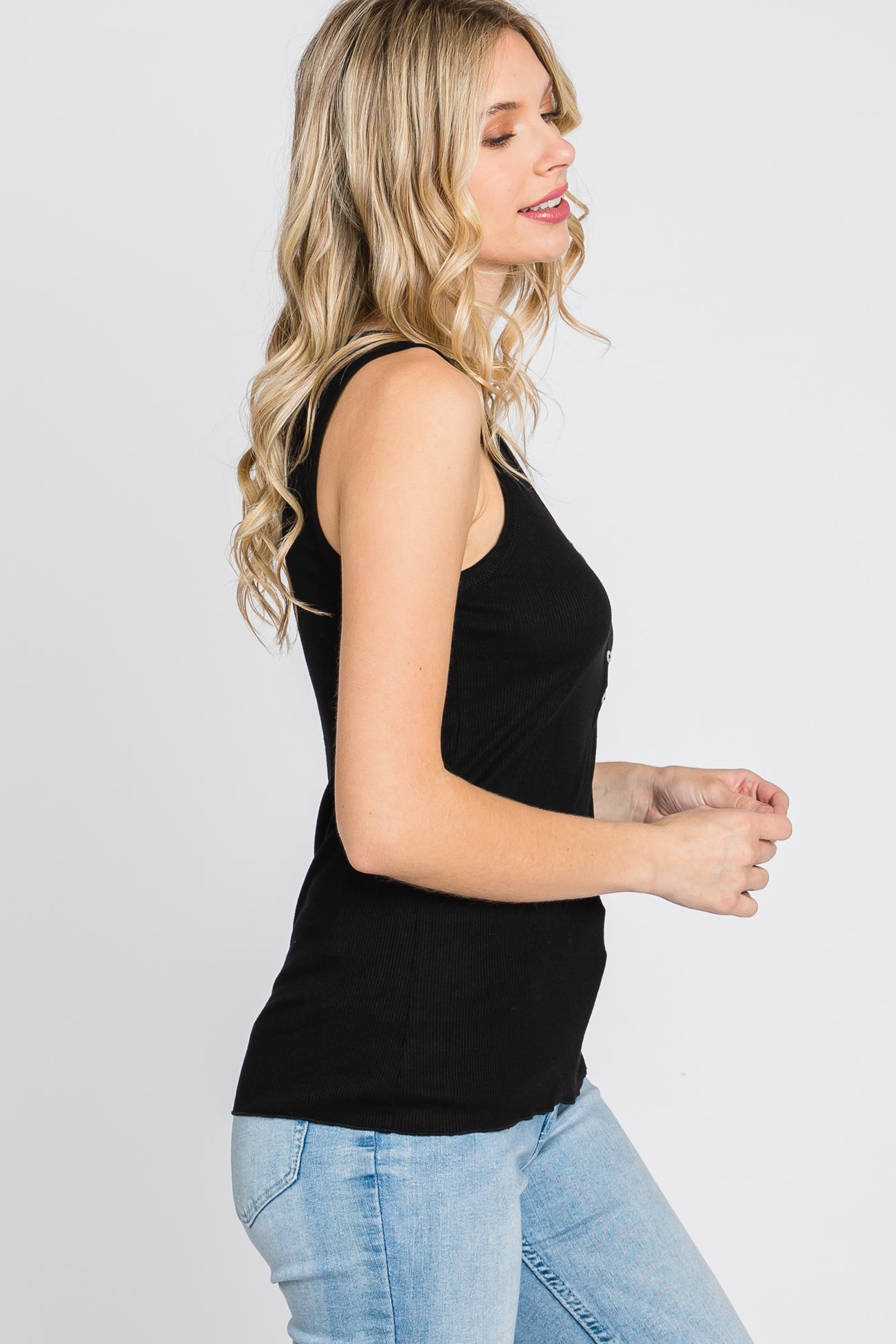 woman wearing a black ribbed tank top paired with light blue jeans, standing sideways with a relaxed pose