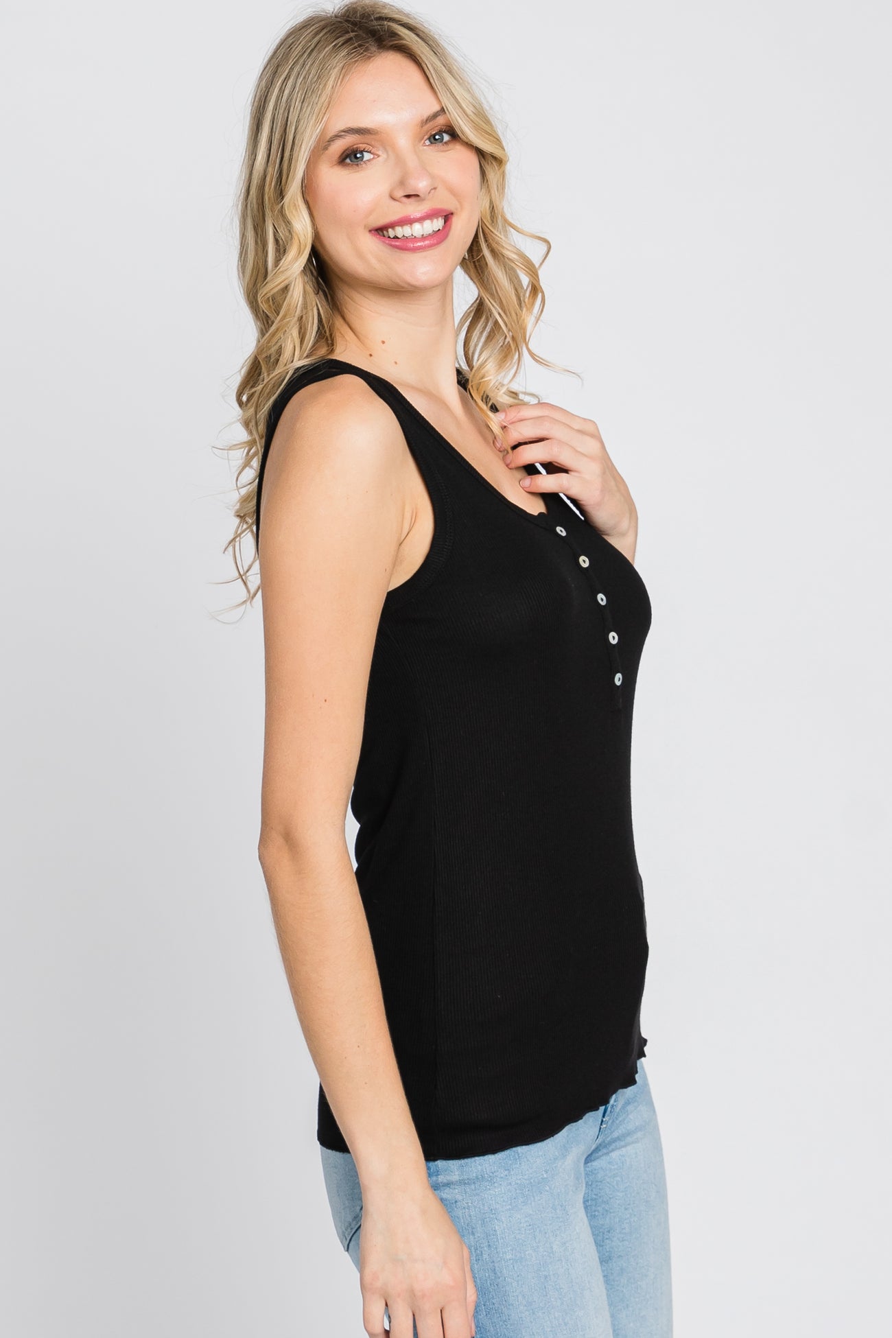 woman wearing a black ribbed tank top with button details and styled with light blue jeans