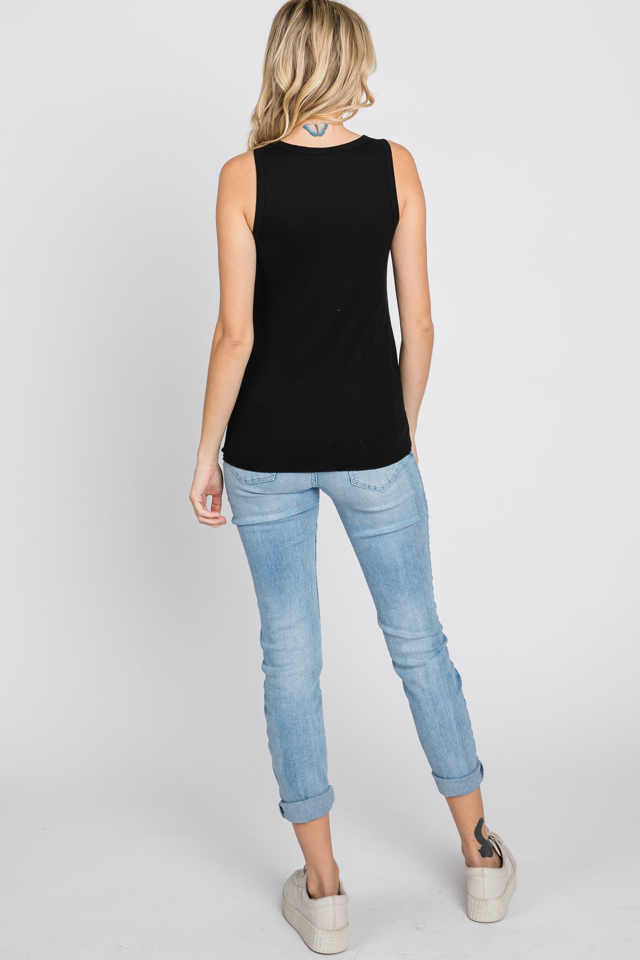 woman wearing a black ribbed tank top and light blue rolled cuff jeans, viewed from the back