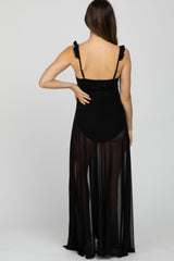 woman wearing a black maternity cover-up dress with ruffled straps, sheer fabric, and a flowy silhouette
