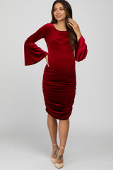 woman wearing a red velvet maternity dress with bell sleeves and side ruching, showing her baby bump