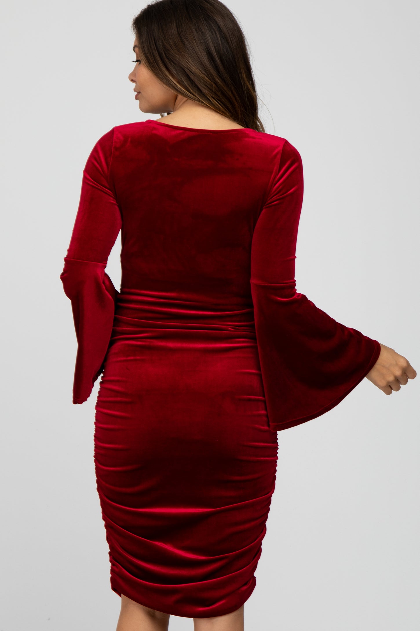 woman wearing a red velvet long sleeve maternity dress with bell sleeves and ruched details at the back