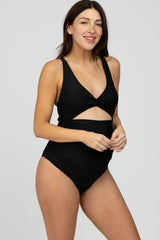 woman wearing a black maternity swimsuit with a twist front design, showing her baby bump