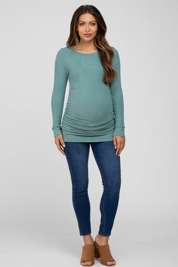 woman wearing a teal long sleeve maternity top with side ruching and blue skinny jeans, showing her baby bump
