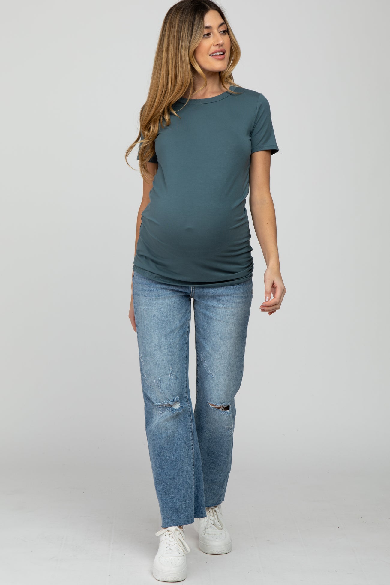 woman wearing a teal maternity t-shirt and distressed blue jeans, showing her baby bump while walking
