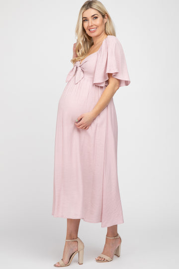 woman wearing a pink maternity dress with tie front detail and flutter sleeves, showcasing her baby bump
