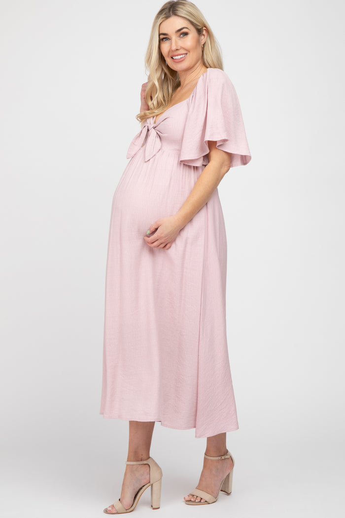 woman wearing a pink maternity dress with tie front detail and flutter sleeves, showcasing her baby bump