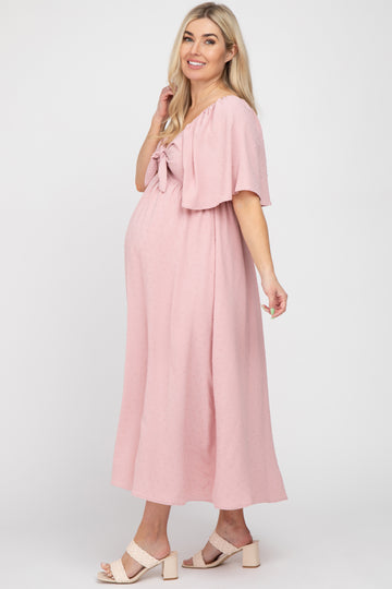 woman wearing a pink maternity dress with a tie-front detail and flutter sleeves, showcasing her baby bump