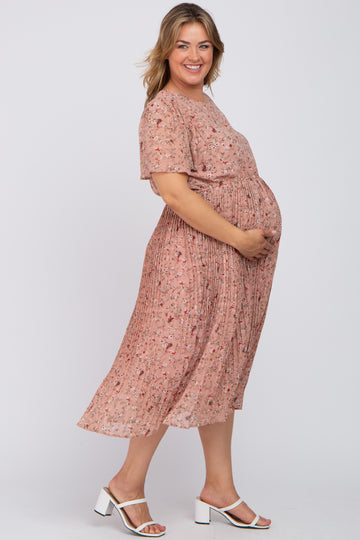 woman wearing a blush floral maternity plus dress with pleats, showcasing her baby bump and smiling to the side