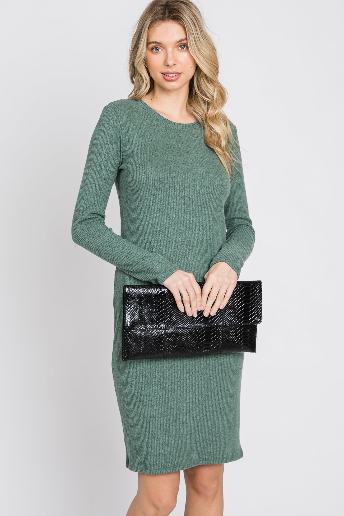 woman wearing a green ribbed knit long sleeve dress and holding a black clutch bag