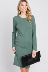 woman wearing a green long sleeve ribbed dress, smiling and holding a black clutch bag