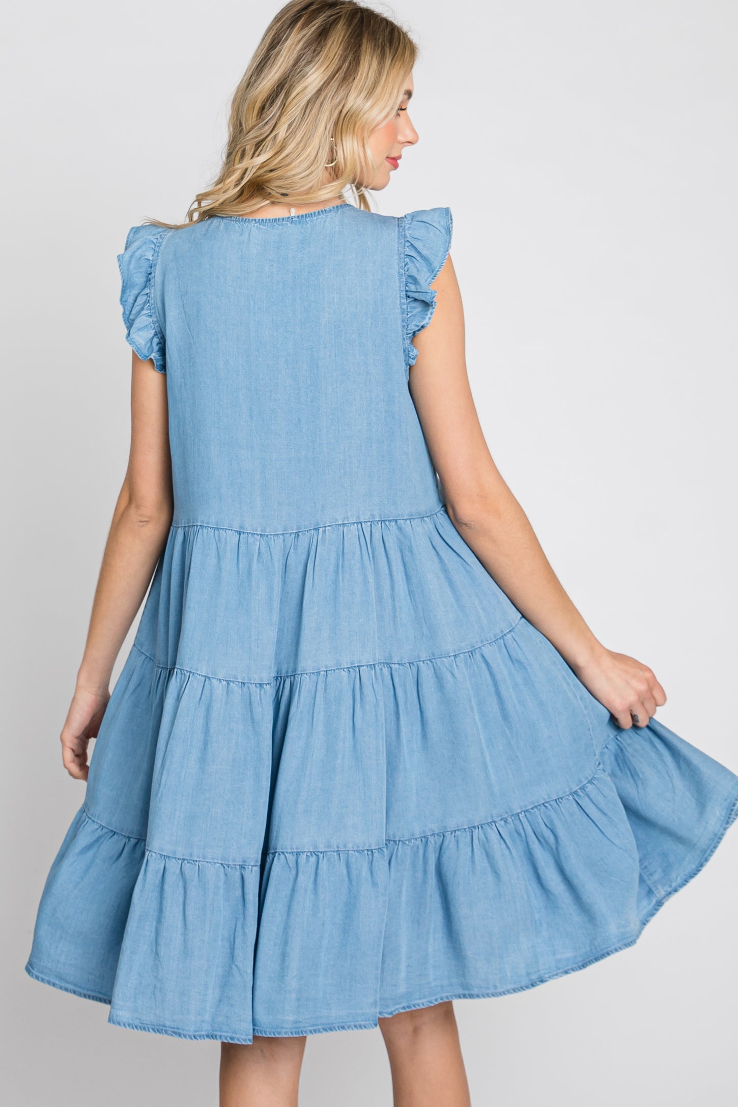 woman wearing a light blue tiered denim dress with ruffled sleeves, twirling to show the back view