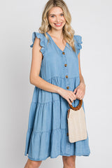 woman wearing a light blue chambray tiered dress with ruffled sleeves and buttons, holding a woven bag
