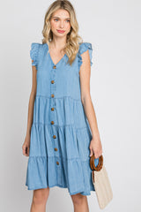 woman wearing a light blue tiered denim dress with ruffled sleeves and button details, holding a small handbag