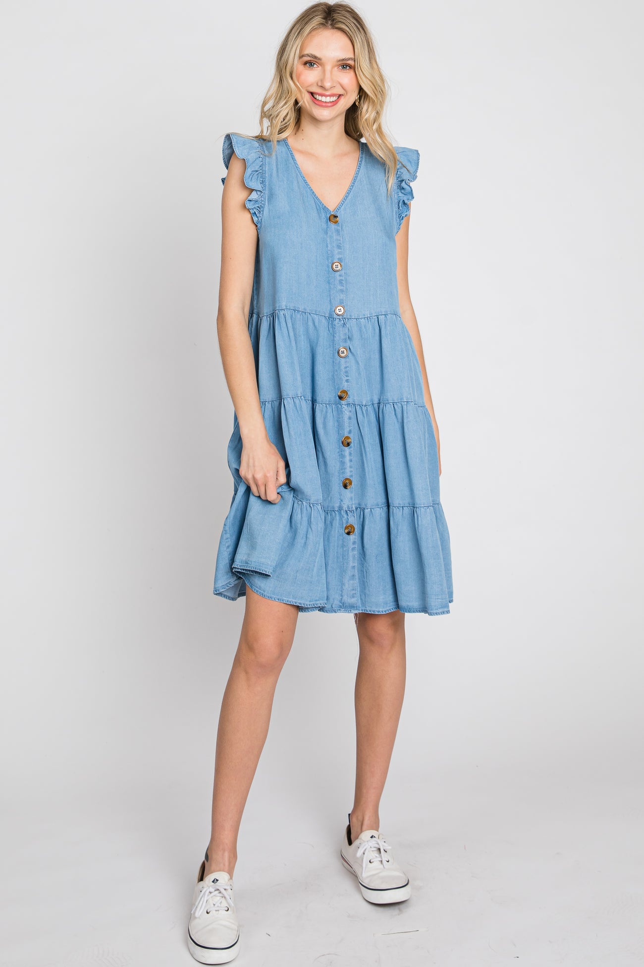 woman wearing a light wash denim tiered mini dress with ruffle sleeves and button front