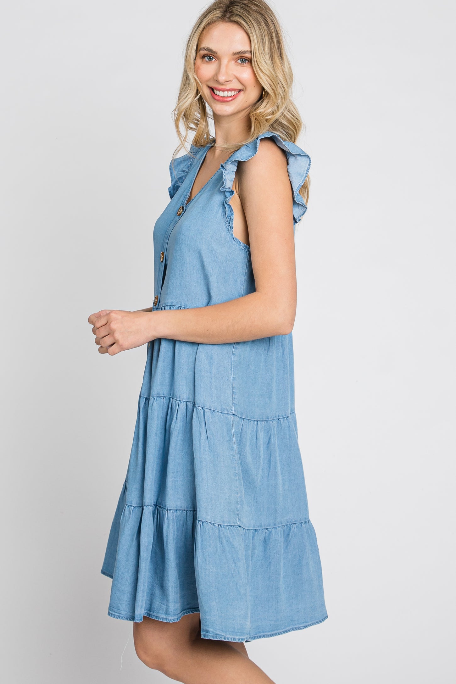 woman wearing a light blue denim dress with ruffle sleeves and tiered skirt, smiling and standing sideways