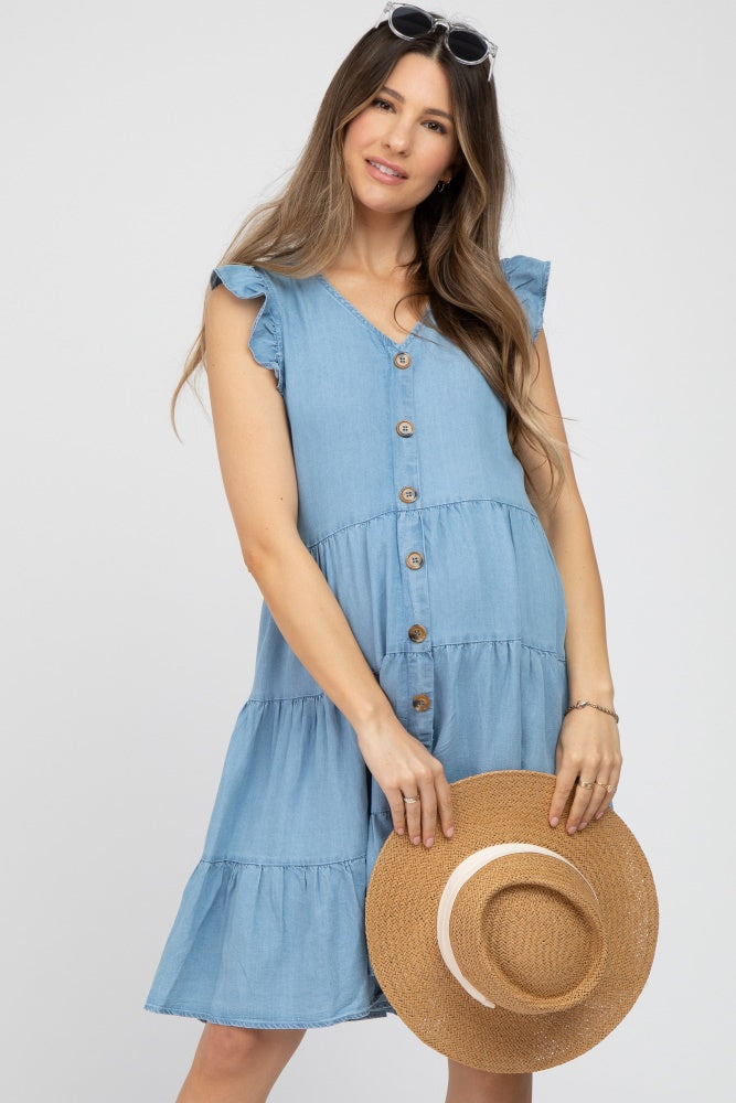 woman wearing a light blue maternity dress with ruffle sleeves and buttons, holding a straw hat, baby bump visible
