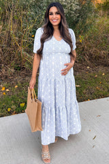 woman wearing a light blue floral maternity maxi dress and holding her baby bump while carrying a tan tote bag