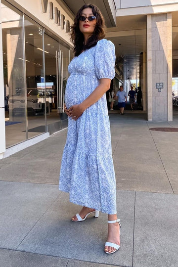 woman wearing a light blue floral maternity maxi dress and holding her baby bump