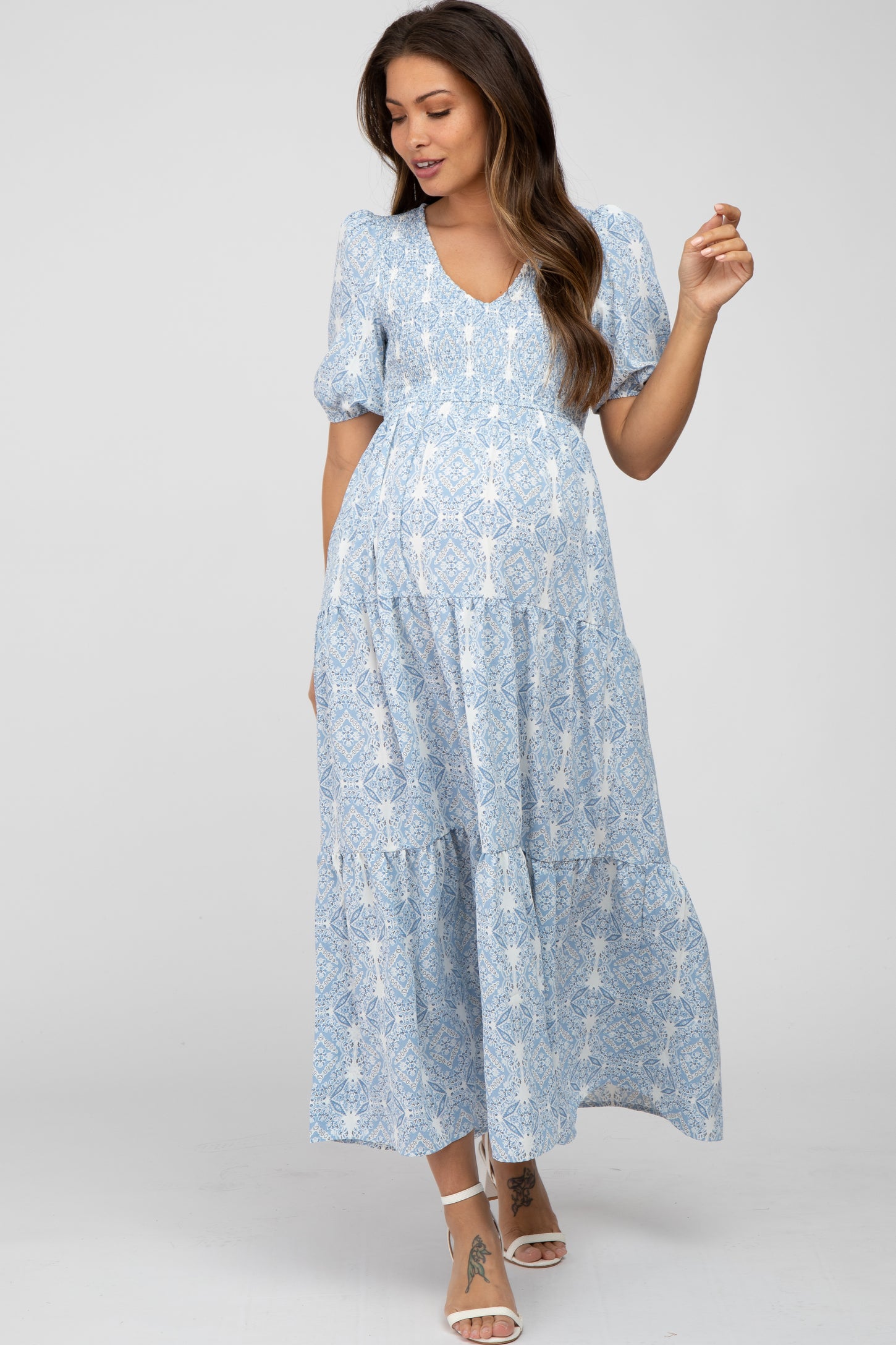woman wearing a light blue maternity maxi dress with a v-neck, puff sleeves, and a tiered skirt, showcasing a baby bump