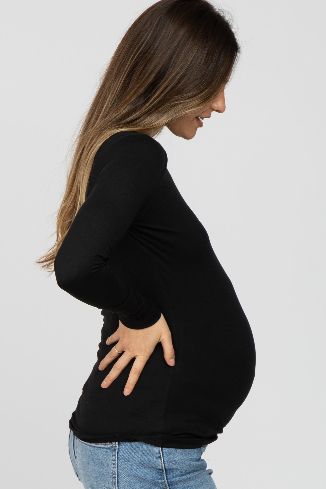 woman wearing a black long sleeve maternity top and showing her baby bump while holding her lower back