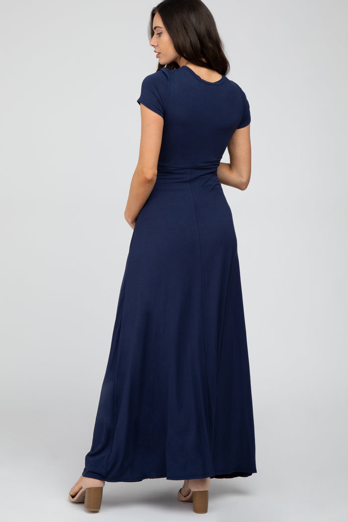 woman wearing a navy blue short sleeve maternity maxi dress showcasing a fitted bodice and flowing skirt