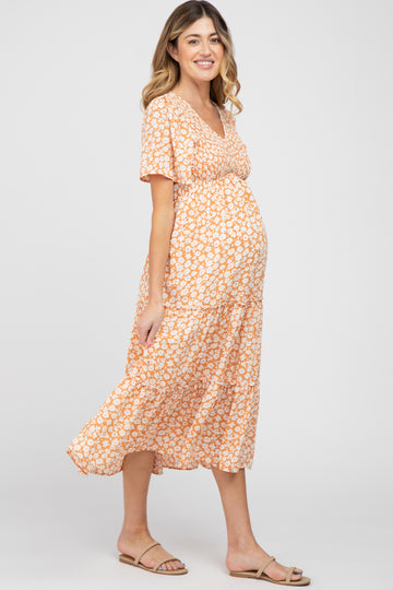 woman wearing a floral orange maternity dress with a tiered skirt and a visible baby bump