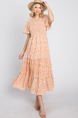 woman wearing orange floral smocked midi dress and straw hat against white background