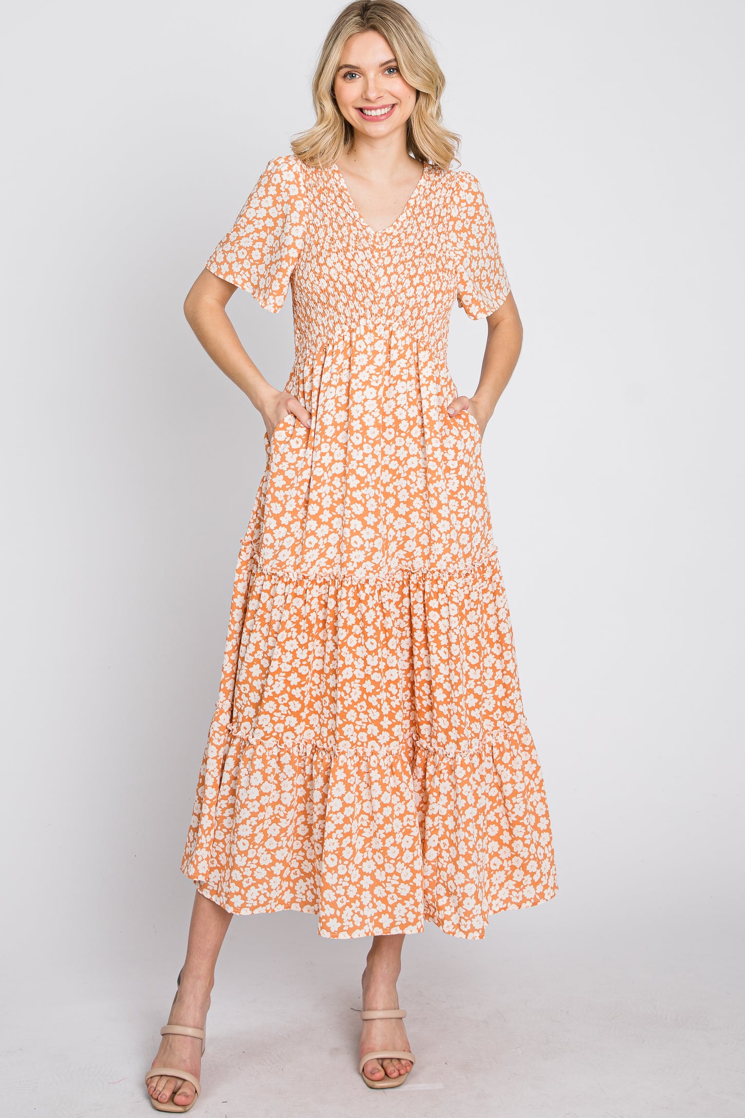 woman wearing a short sleeve orange floral maxi dress with a tiered skirt and pockets, smiling at the camera