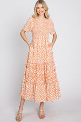 woman wearing a short sleeve orange floral maxi dress with a tiered skirt and pockets, smiling at the camera