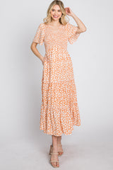 woman wearing orange and white floral print tiered maxi dress with smocked bodice and flutter sleeves