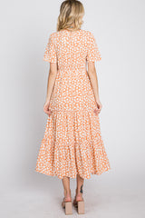 woman wearing an orange floral print maxi dress with short sleeves and a tiered skirt, viewed from the back