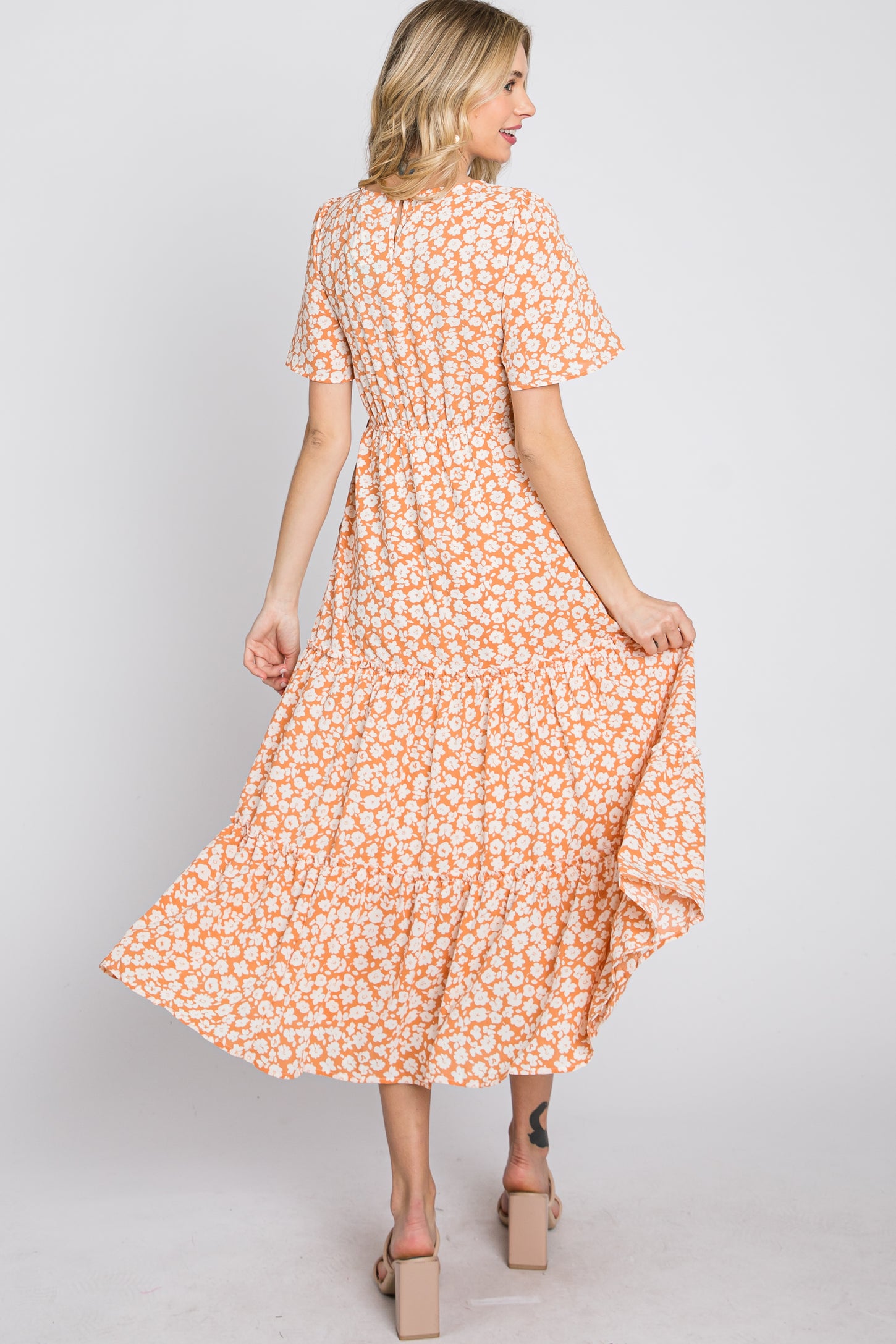 woman wearing an orange floral maxi dress with short sleeves and a tiered skirt, seen from the back