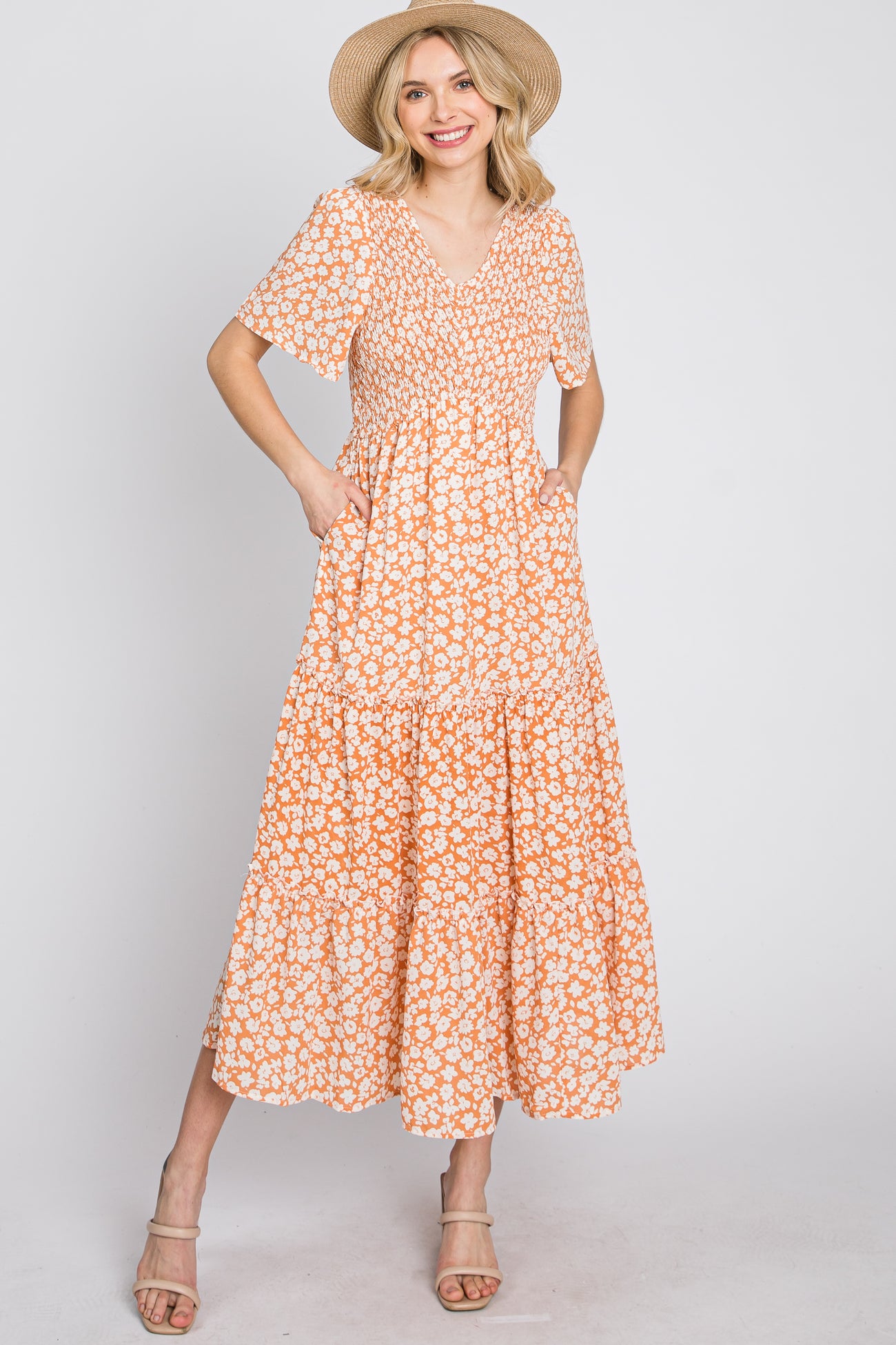 woman wearing an orange floral maxi dress with short sleeves and pockets, styled with a straw hat