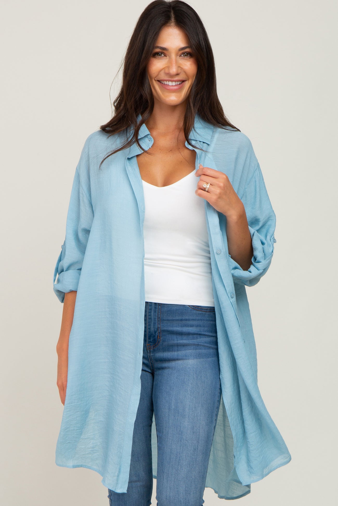 woman wearing a light blue longline button down shirt over a white tank top and blue jeans