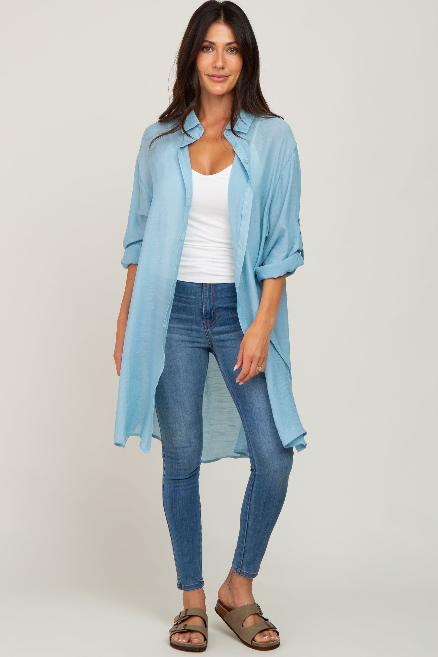 Woman wearing a light blue longline button-down shirt over a white tank top and blue skinny jeans