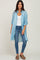 Woman wearing a light blue longline button-down shirt over a white tank top and blue skinny jeans