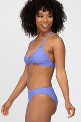 woman wearing a lavender bikini with a triangle top and minimal coverage bottoms, smiling and posing to the side