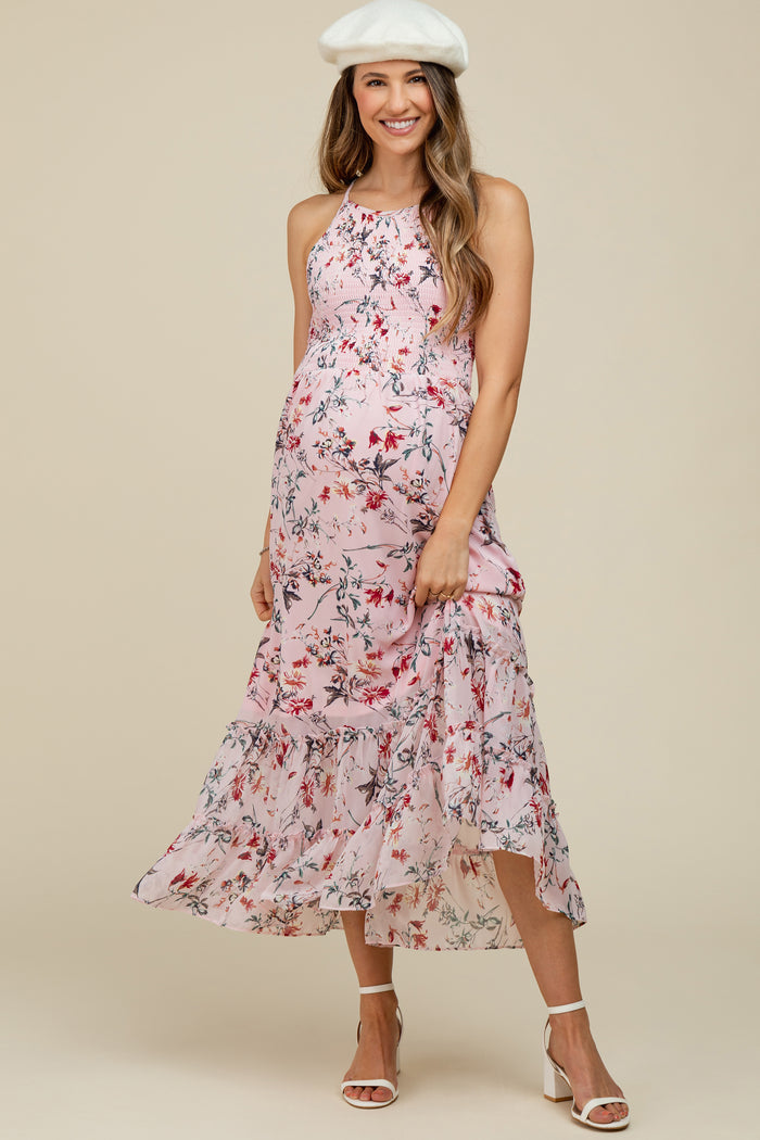 Smiling pregnant woman in a pink floral maternity maxi dress and white beret against a beige background